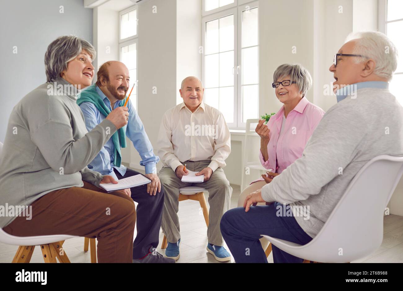Cheerful elderly people are talking at psychological therapy in nursing home. Stock Photo