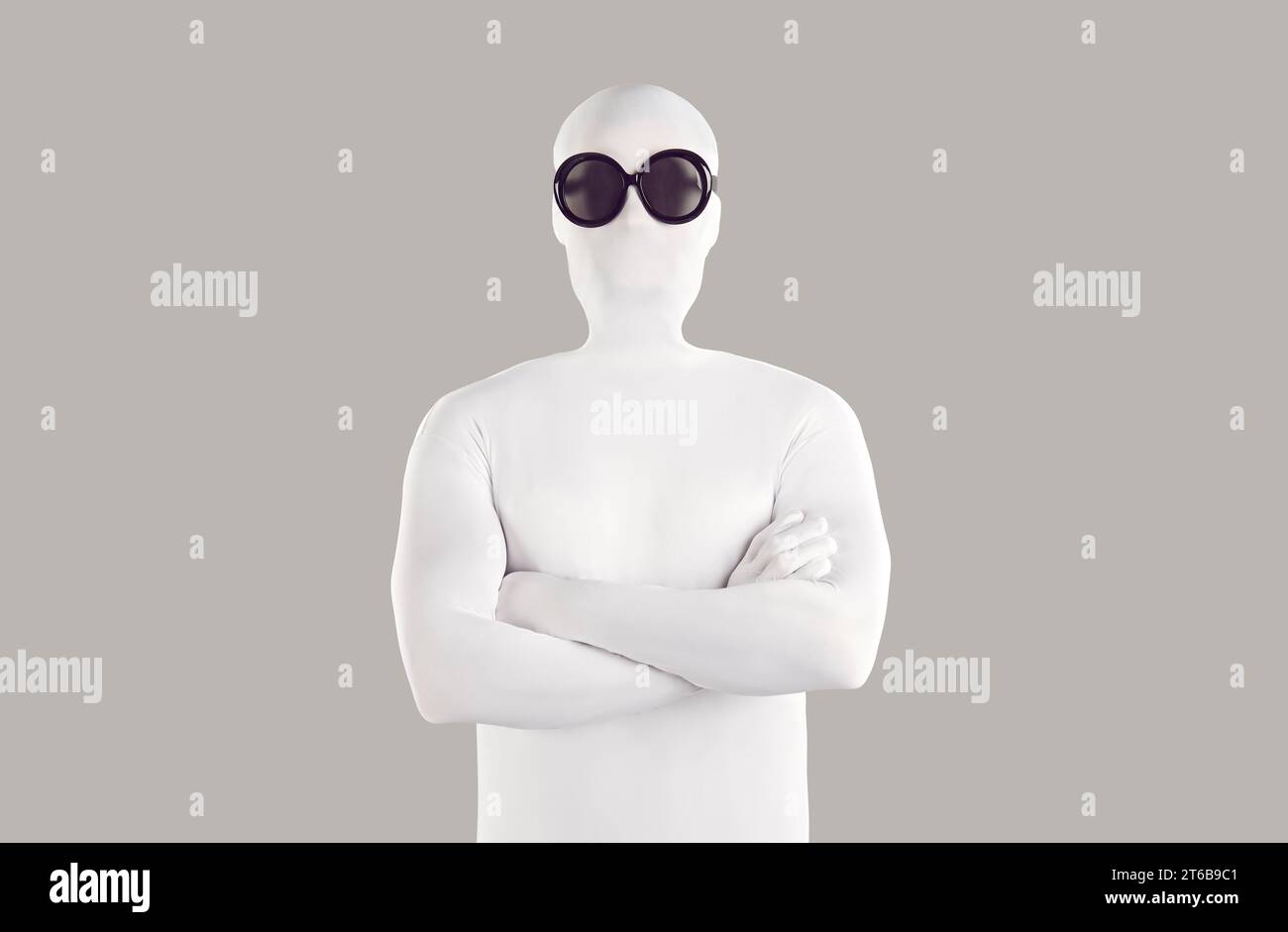 Portrait of man disguised in white bodysuit and black sunglasses standing with folded arms Stock Photo
