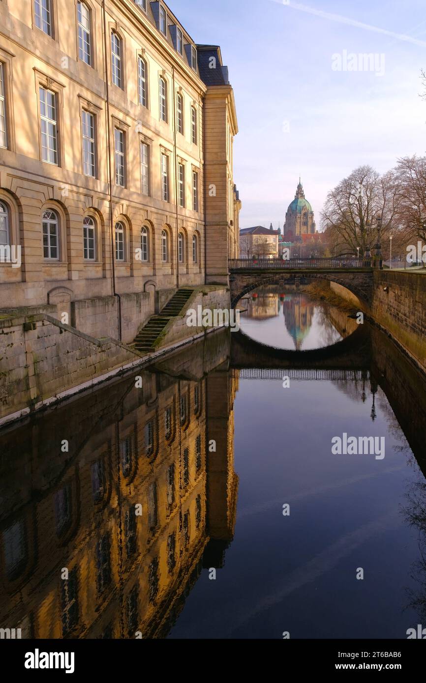 An arched concrete bridge extending across a tranquil blue body of water with a modern building in the background Stock Photo