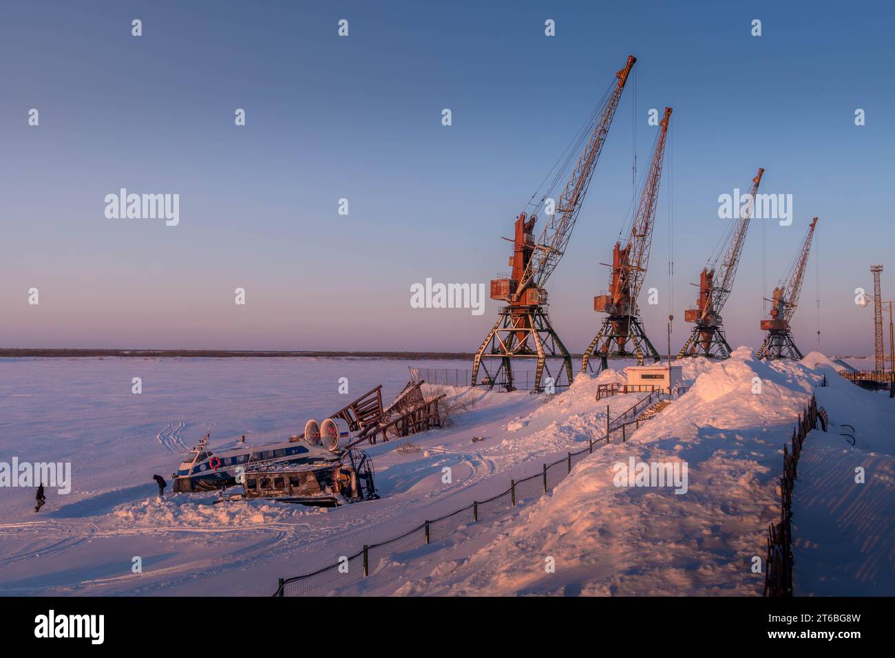 The snow-covered port cranes and snow piles on the frozen Pechora river bank at Naryan-Mar, the northern Russian Nenets Autonomous Region. Stock Photo
