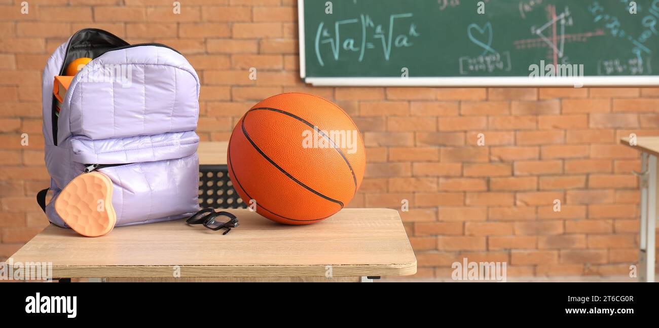 School backpack and ball on desk in classroom Stock Photo