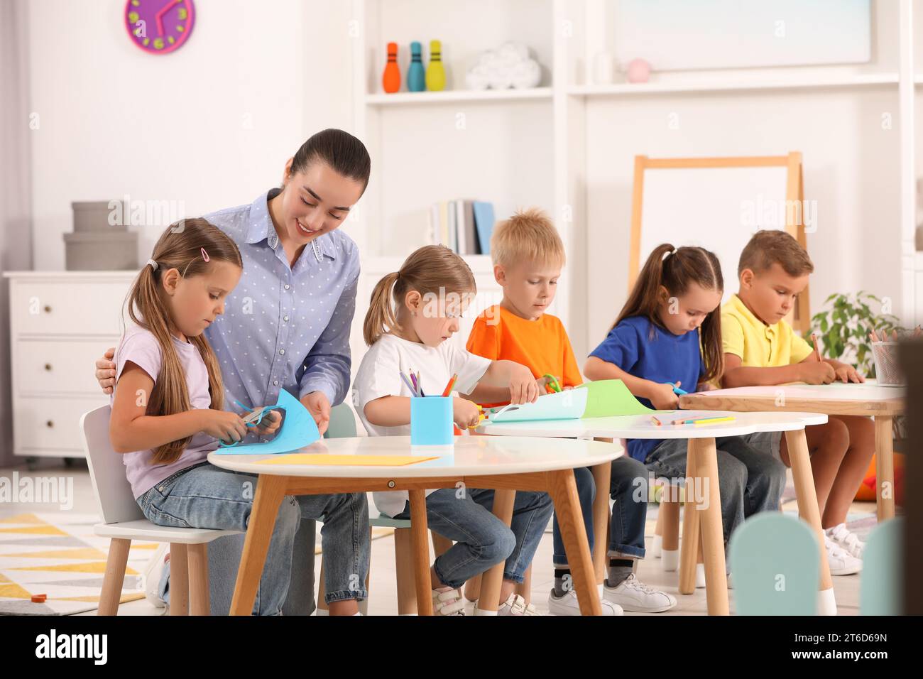Nursery teacher with group of cute little children drawing and cutting