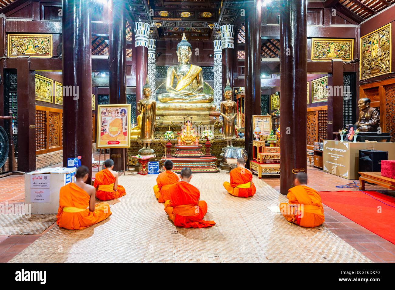 Chiang Mai,Thailand-March 20 2023: Illuminated by lights inside the ancient teak wood structure,monks chant during evening prayers,before the golden B Stock Photo