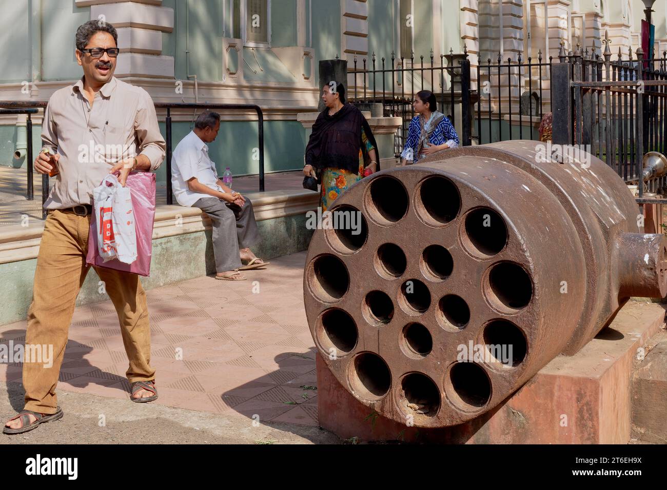 Visitors to Dr. Bhau Daji Lad Museum in Byculla, Mumbai, India, next to a large multi-barrel cannon from the Mughal era placed outside of the museum Stock Photo