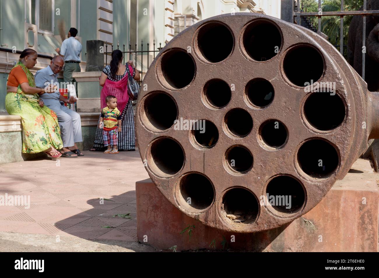Visitors to Dr. Bhau Daji Lad Museum in Byculla, Mumbai, India, next to a large multi-barrel cannon from the Mughal era placed outside of the museum Stock Photo
