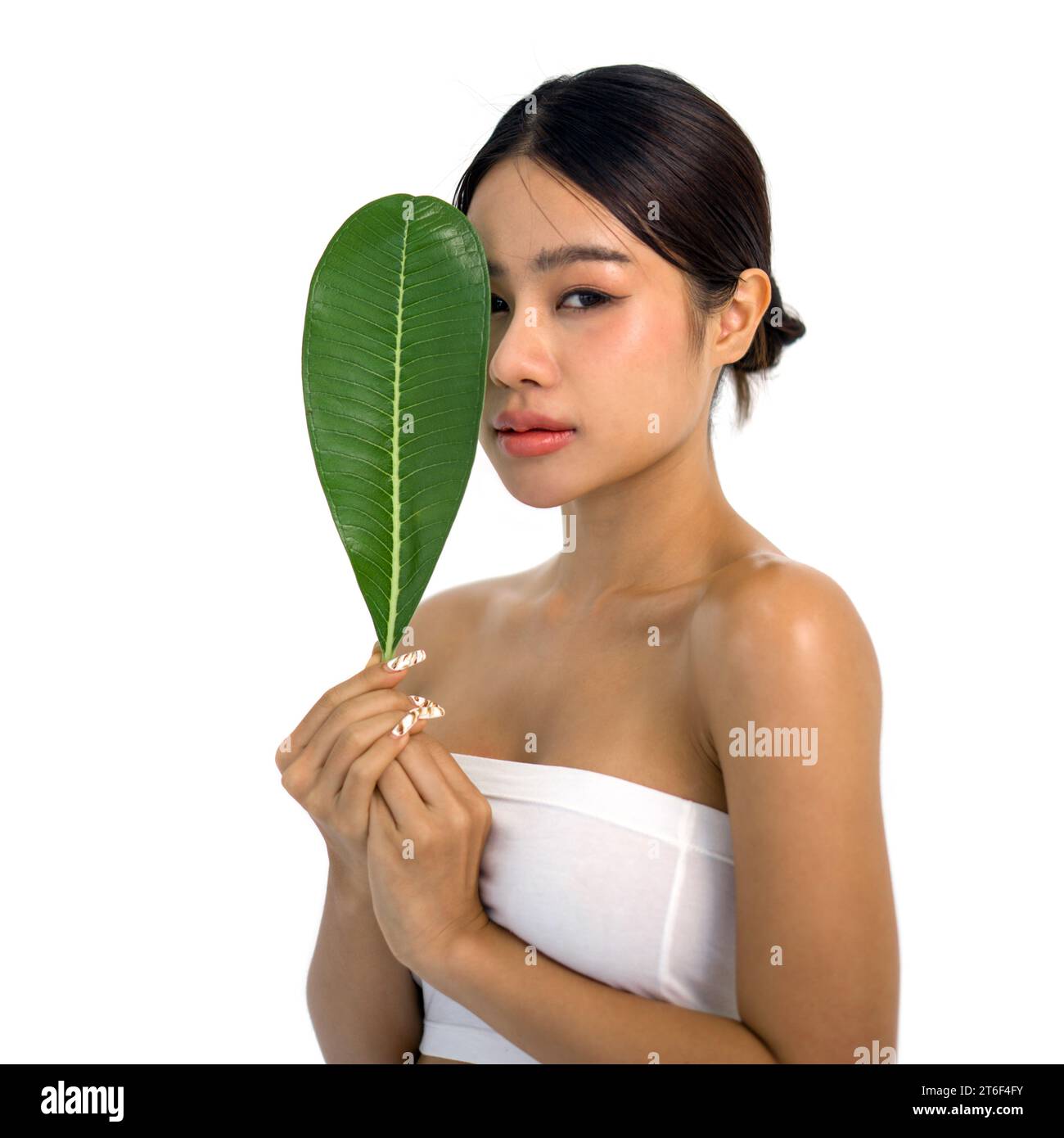 Young asian woman playfully covering her face with a vibrant green leaf ...