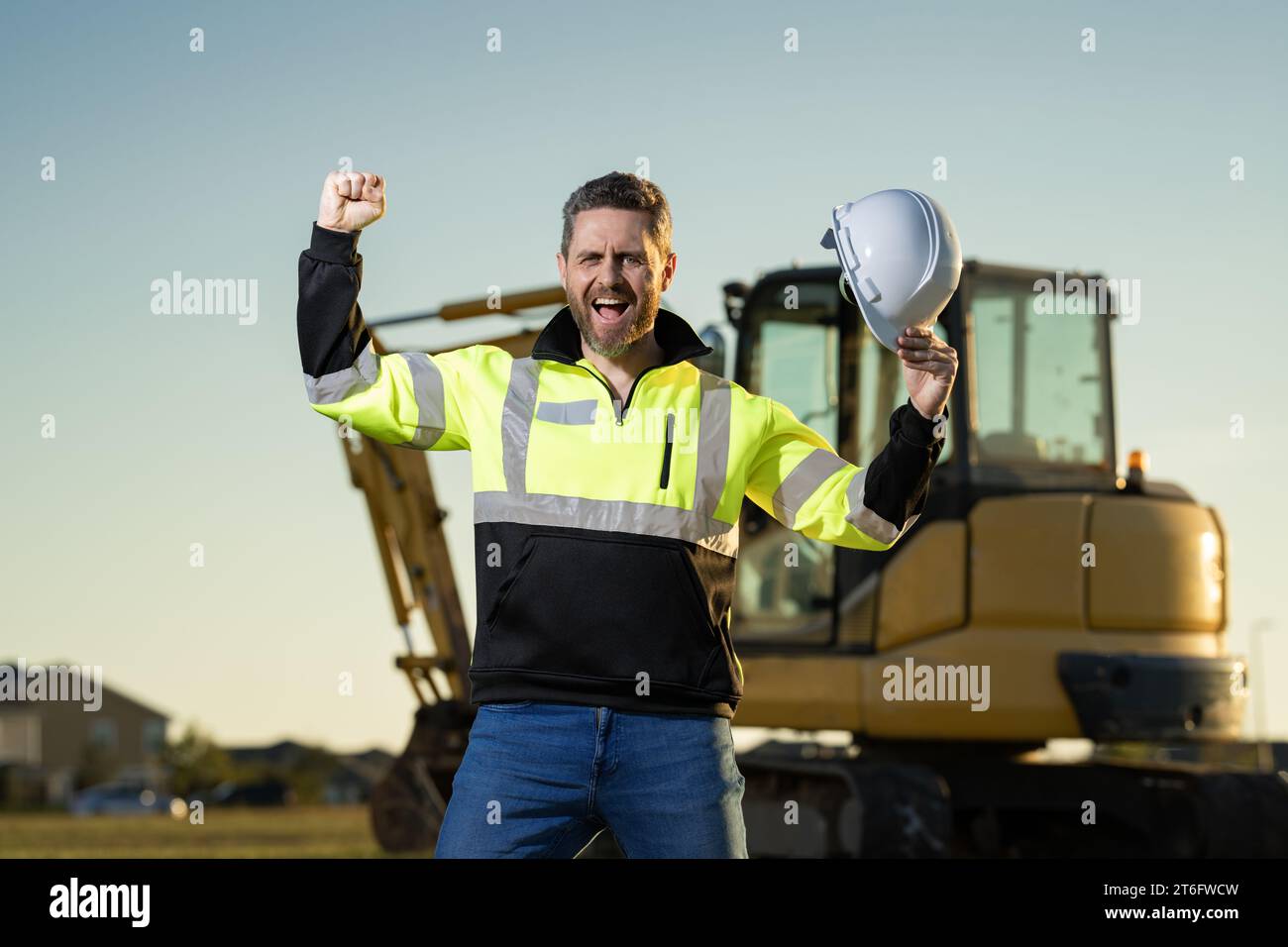 Construction man industry with excavator at industrial site. Worker in helmet build with bulldozer. Engineer work with builder contractor in hardhat. Stock Photo