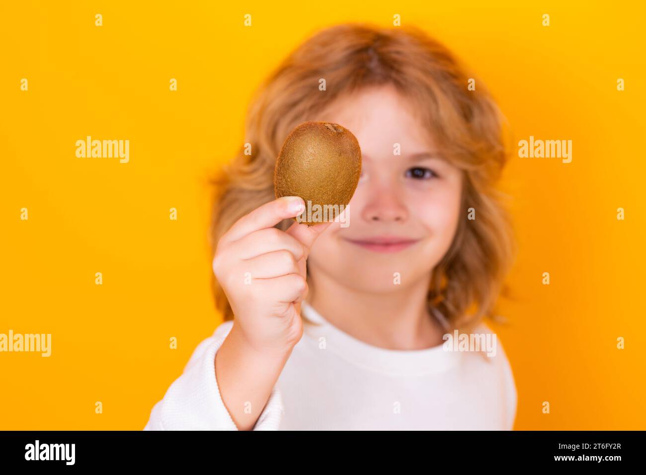 Vitamin and healthy fruits for kids. Child hold kiwi in studio. Kiwi fruit. Studio portrait of cute kid boy with kiwi isolated on yellow Stock Photo
