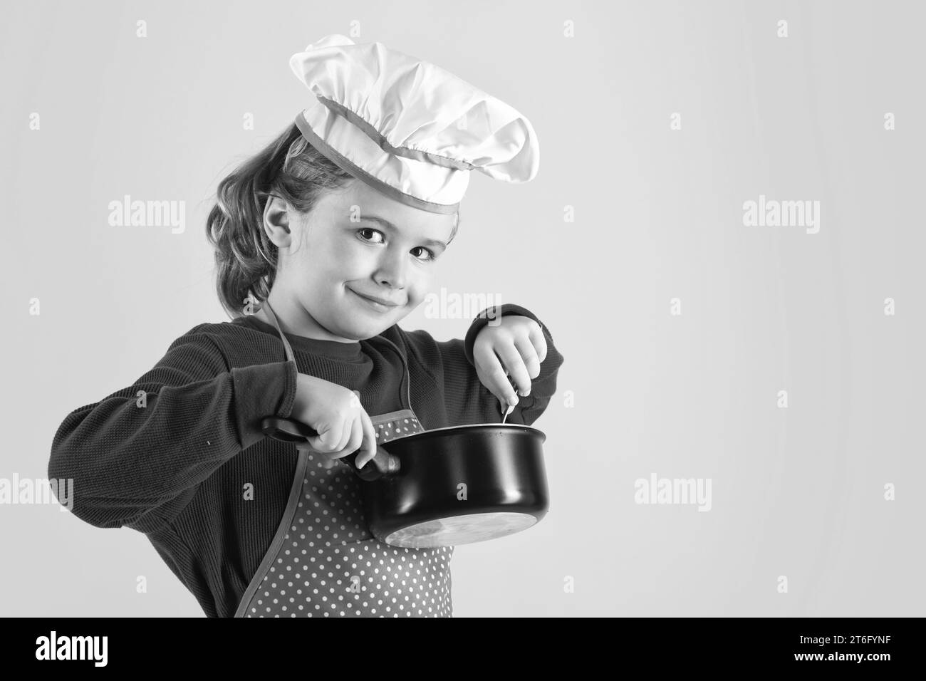 Kid chef cook with cooking pot stockpot. Excited chef cook. Child wearing cooker uniform and chef hat preparing food, studio portrait Stock Photo