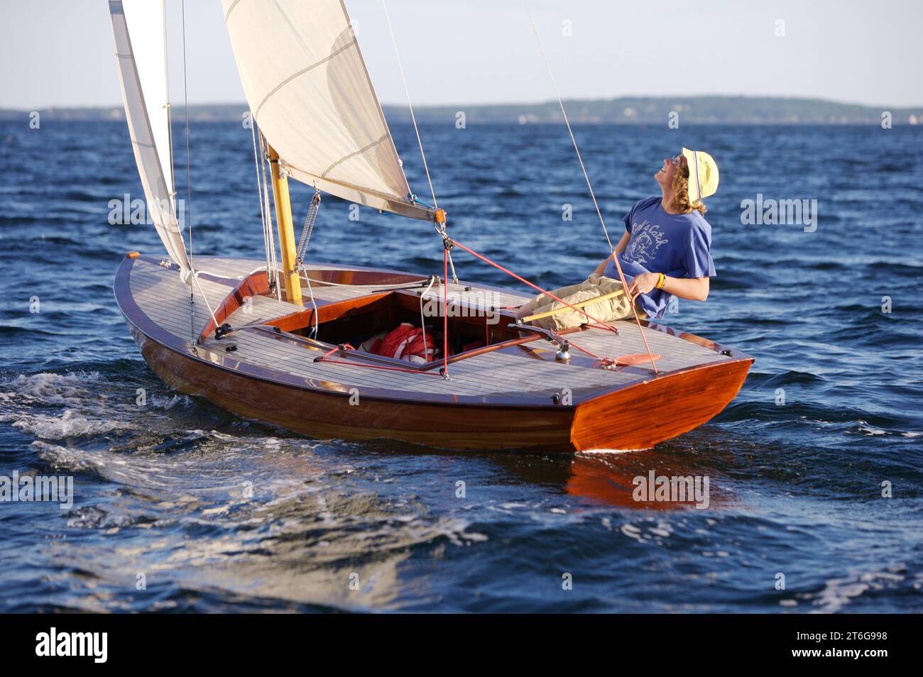 A teenage boy at the helm of a classic wooden sailing dinghy, hikes out