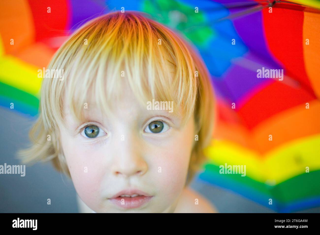 A blond-haired boy under a luminescent, rainbow-colored umbrella. Stock Photo