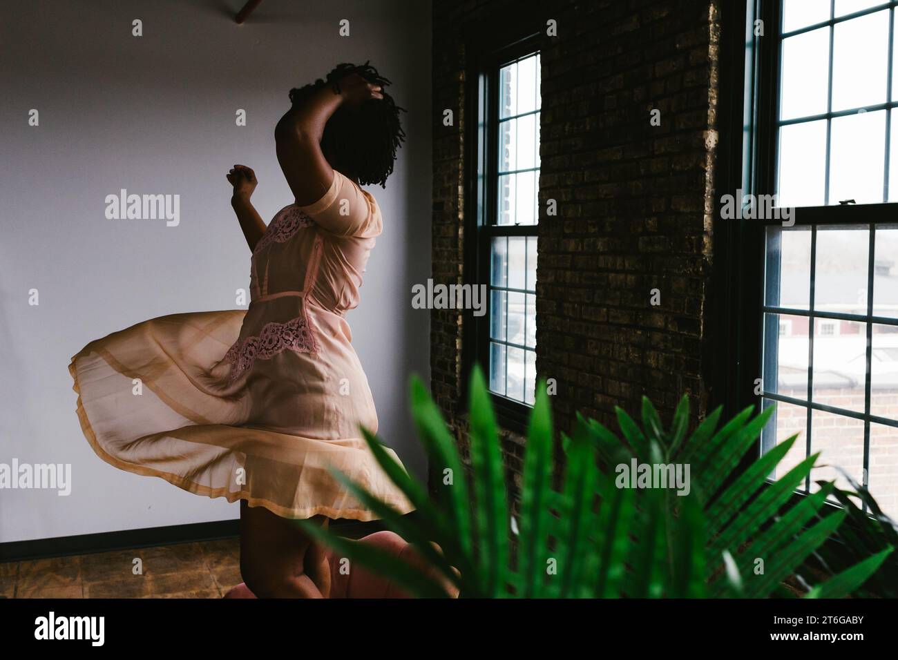 Female dancer twirls in dress in building with brick and windows Stock Photo
