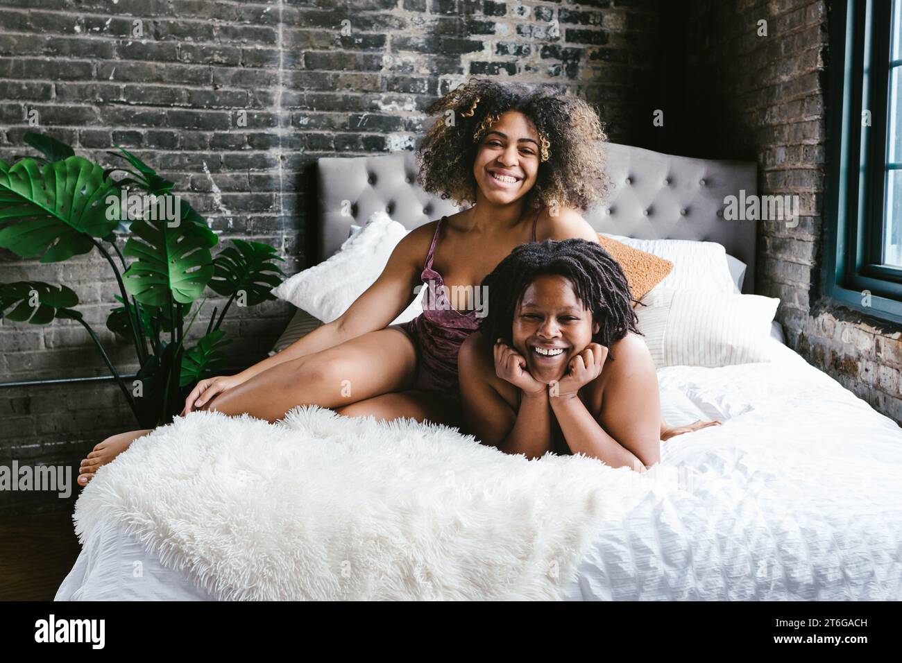 Two mixed race female dancers smile together on bed in apartment Stock