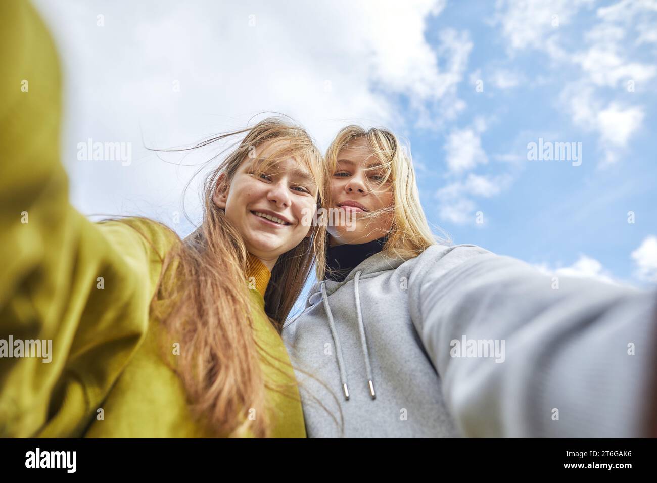 two playful teenage girls posing for a selfie against sky Stock Photo