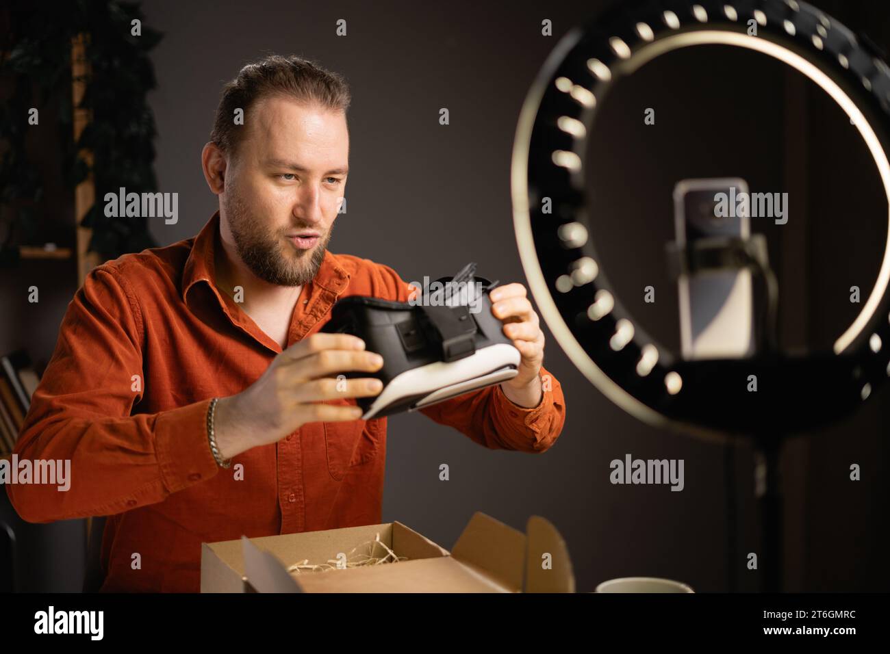 Attractive male blogger promoting model of VR Goggles and recommending innovative product, filming video review of modern gadget at home. Influencer Stock Photo