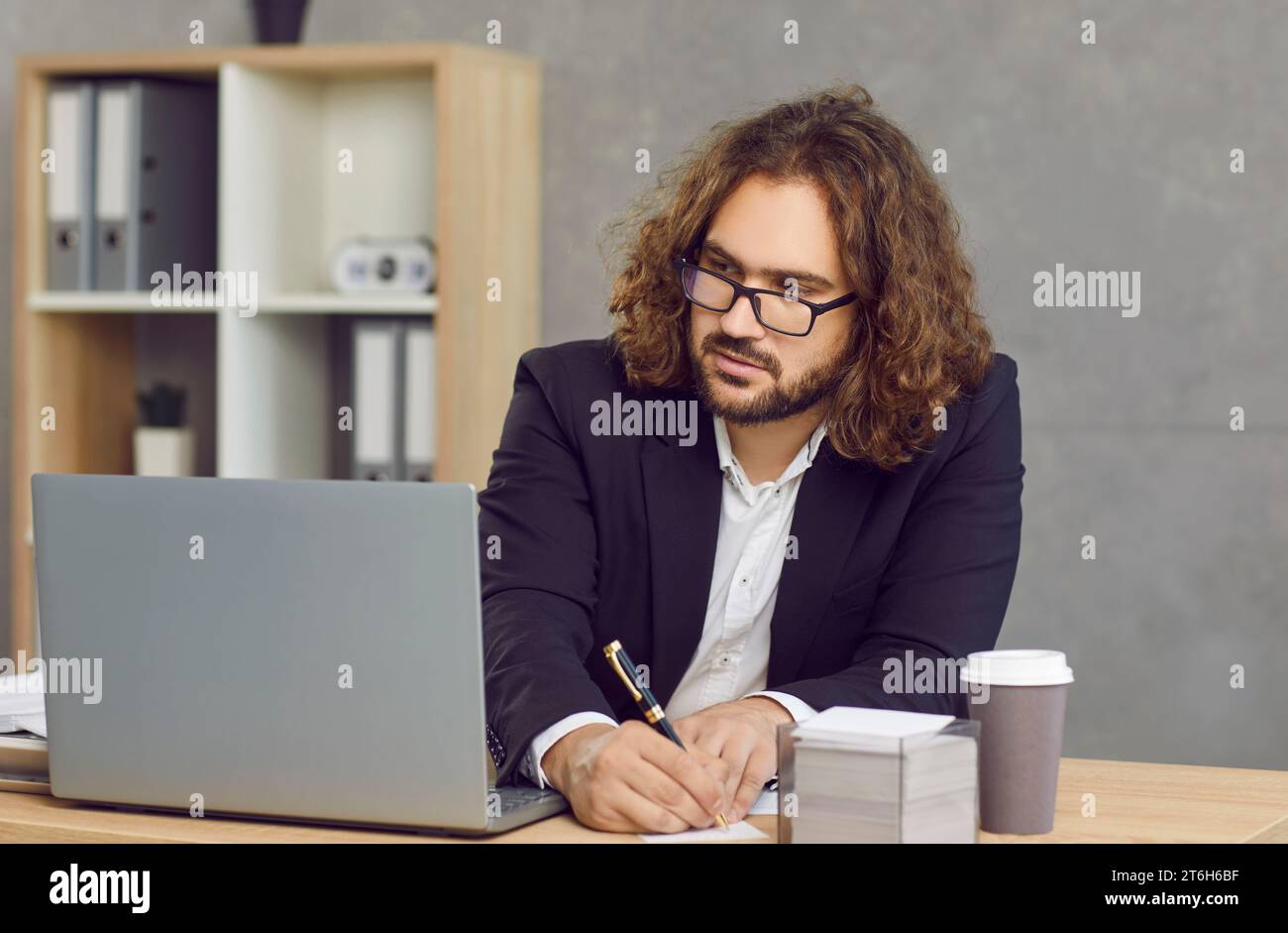 Young businessman sitting at office desk, using laptop computer and taking notes Stock Photo