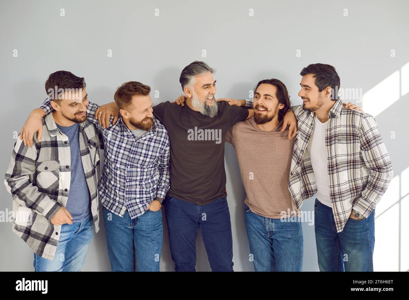 Male bearded friends looking cheerful to each other and smiling on grey ...