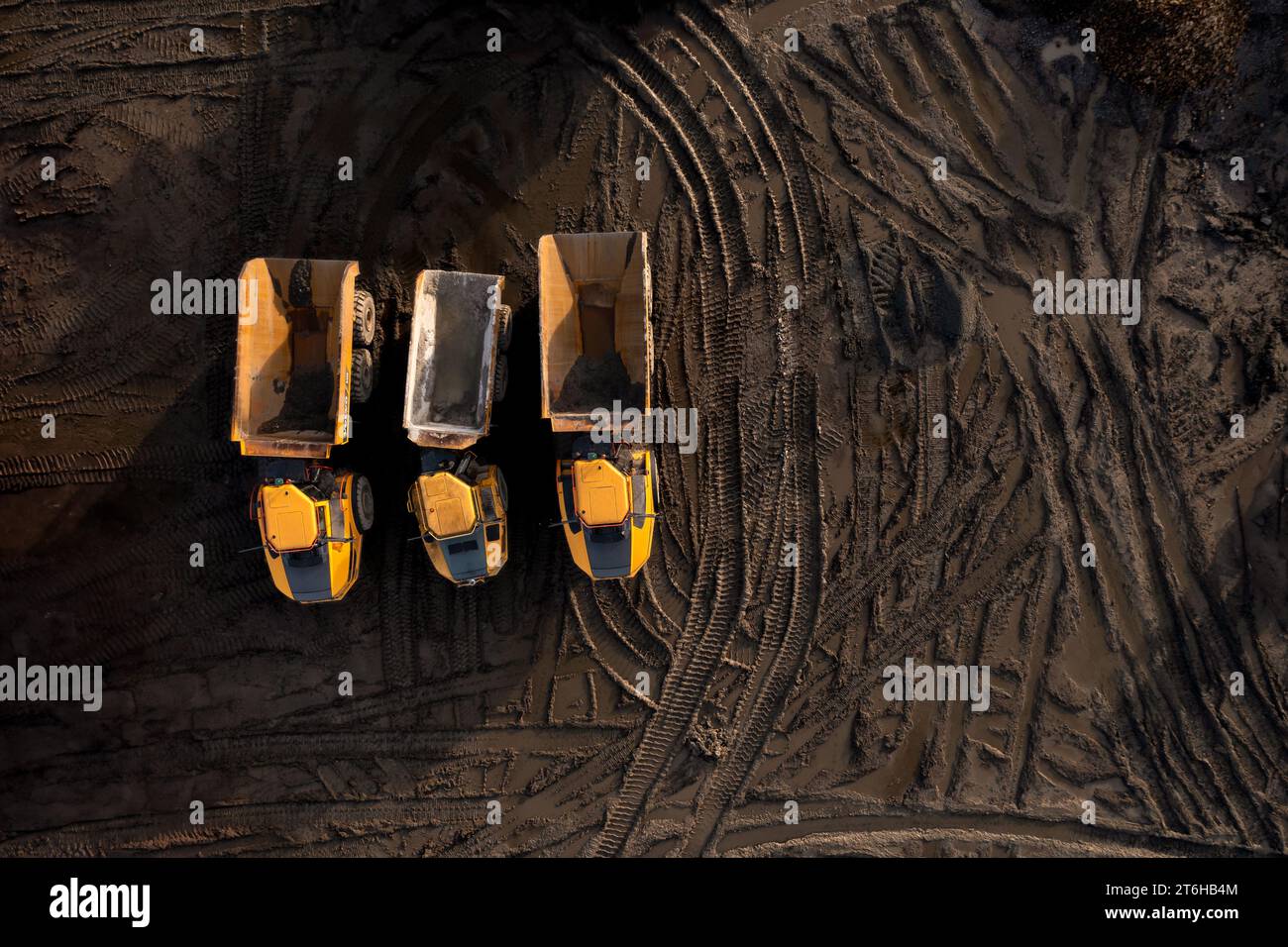 Aerial view directly above industrial dumper truck or earth mover vehicle with muddy soil and tyre tracks in the construction industry on a brownfield Stock Photo