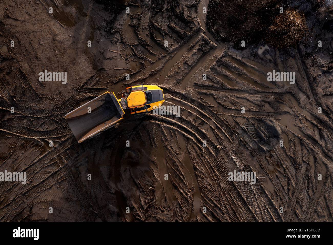 Aerial view directly above an industrial dumper truck or earth mover vehicle with muddy soil and tyre tracks in the construction industry on a brownfi Stock Photo