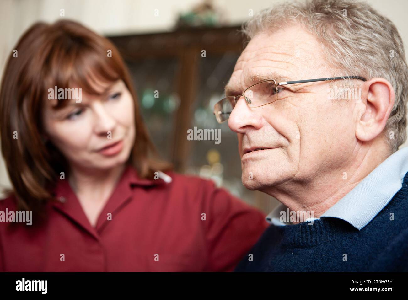 Help the Aged: Home Care. A concerned look on the face of a senior man under the supervision of a visiting care worker. From a series of related image Stock Photo