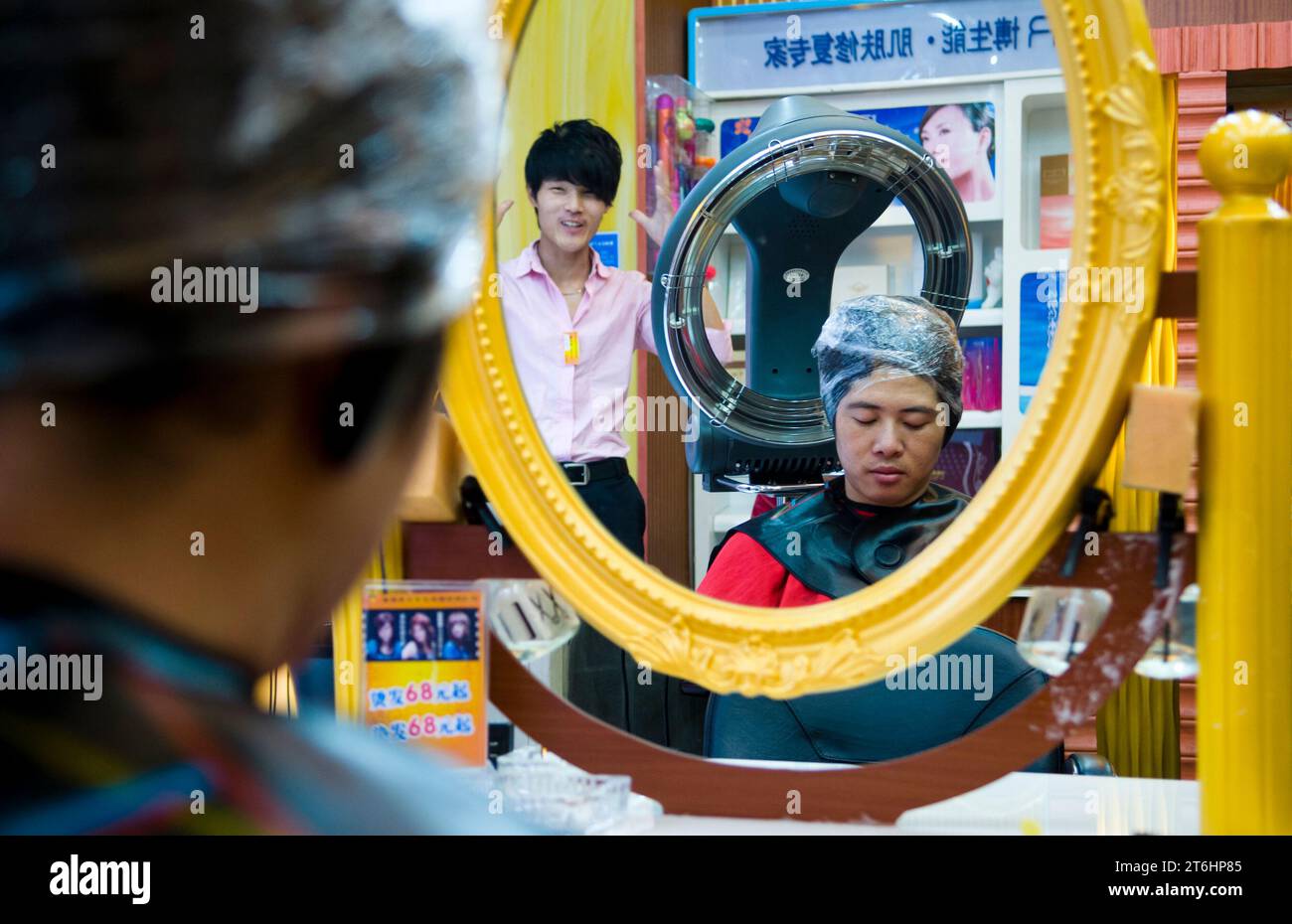 China, Shanghai, Hairdresser in Sichuan Lu, young man under dryer hood, his hairdresser looking on Stock Photo