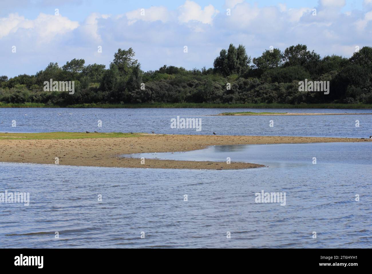 Water surface with small sand island, blue sky in background Stock Photo