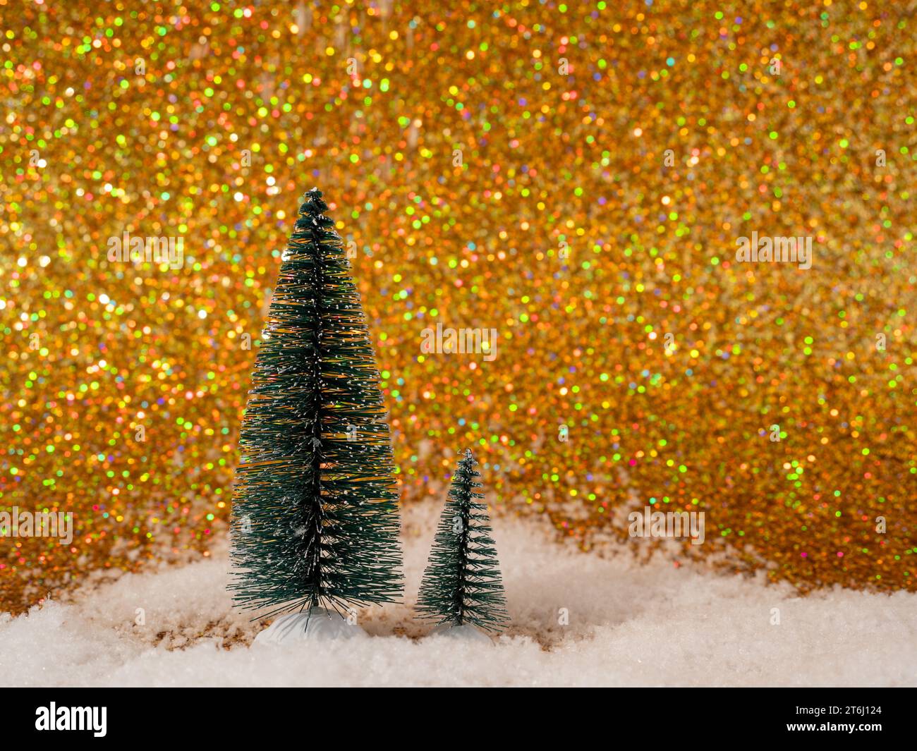 The photo shows a festive scene with decorative artificial Christmas trees set on shiny white snow. The backdrop features a shimmering gold backdrop t Stock Photo