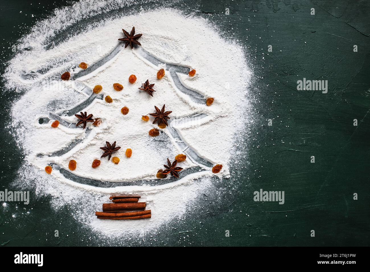 Christmas tree with star of anise, sultans or yellow raisins, and cinnamon bark on a white flour over green background. Table top view Stock Photo