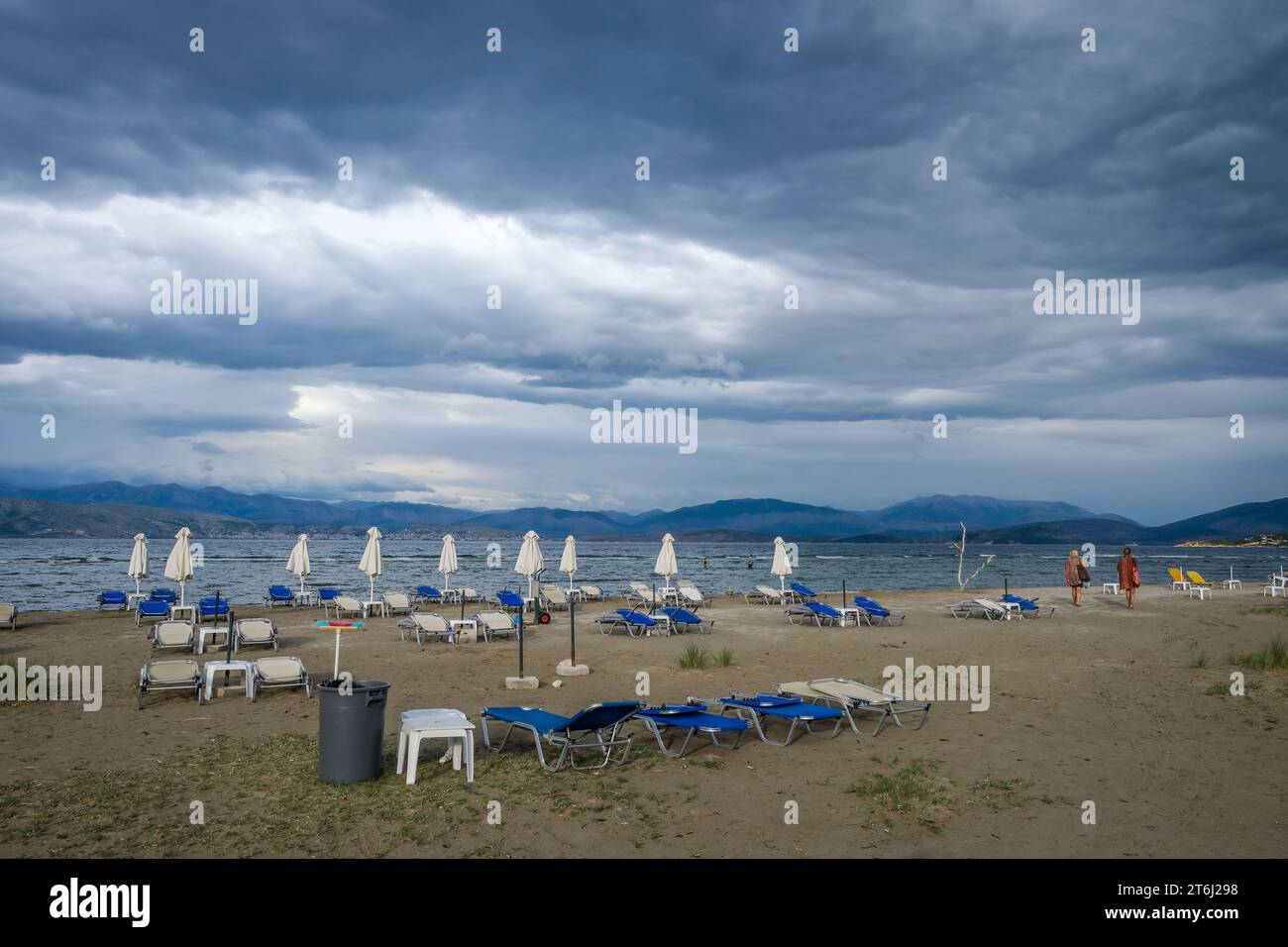 Kalamaki, Corfu, Greece, sun beds and umbrellas at Kalamaki beach in the northeast of the Greek island of Corfu, in the background the mainland of Albania with the seaside resort of Saranda. In front forgotten children's toys, bucket and shovel. Price board umbrella and sun lounger rental. Stock Photo