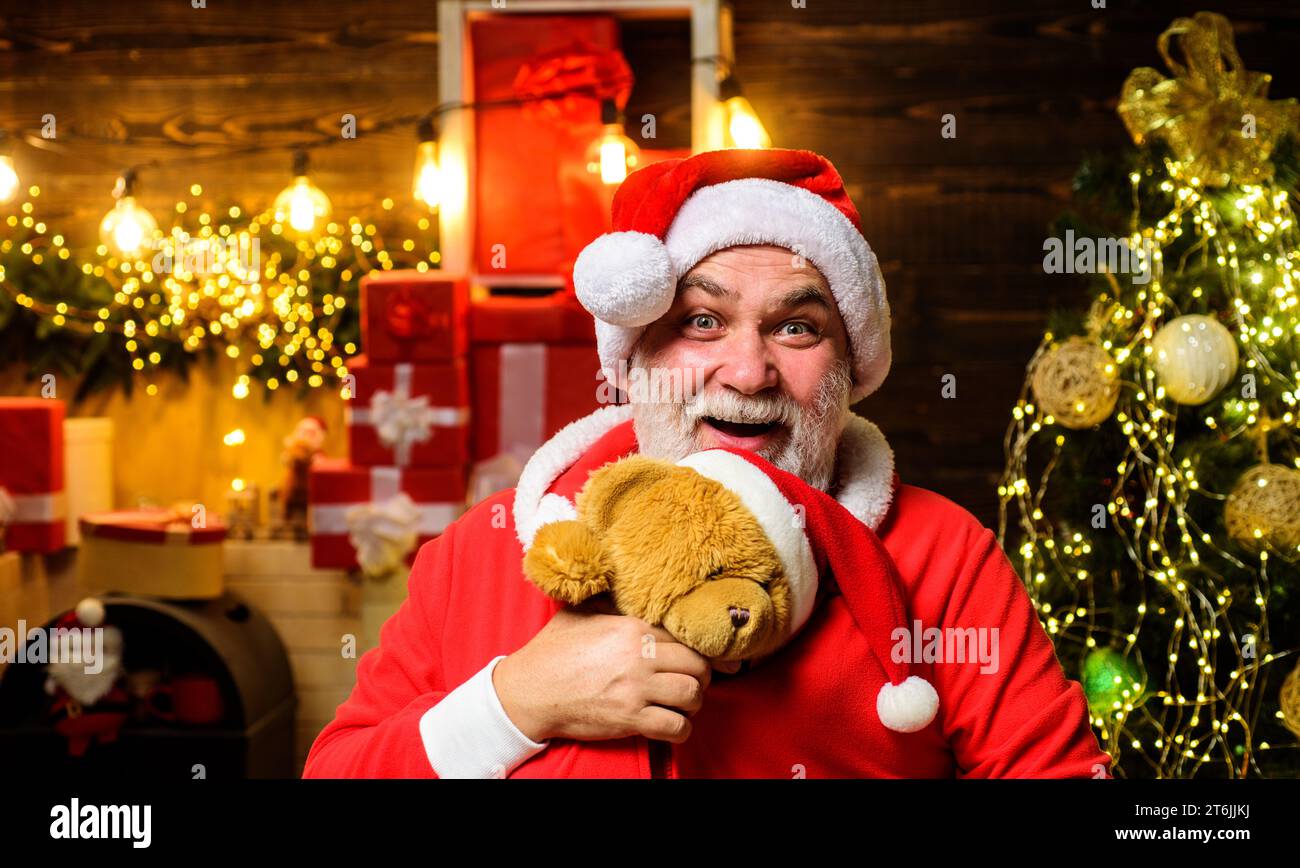 Christmas or New Year holidays. Happy Santa Claus with teddy bear in room decorated for Christmas. Bearded man in Santa costume with teddy bear Stock Photo