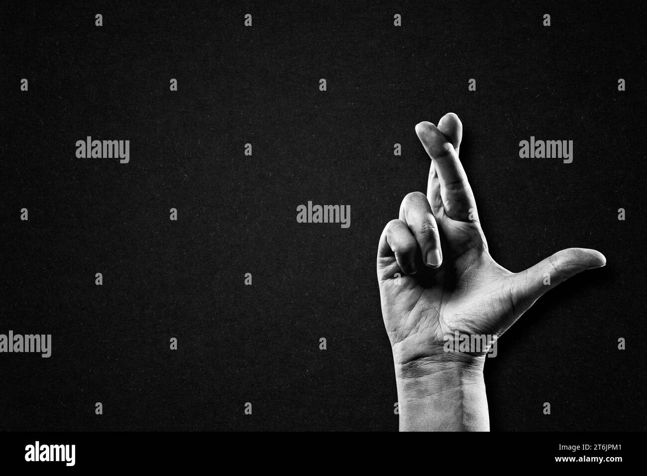 Hand with Crossed Fingers Sign in Black and White on Textured Paper Background, Copy Space Stock Photo