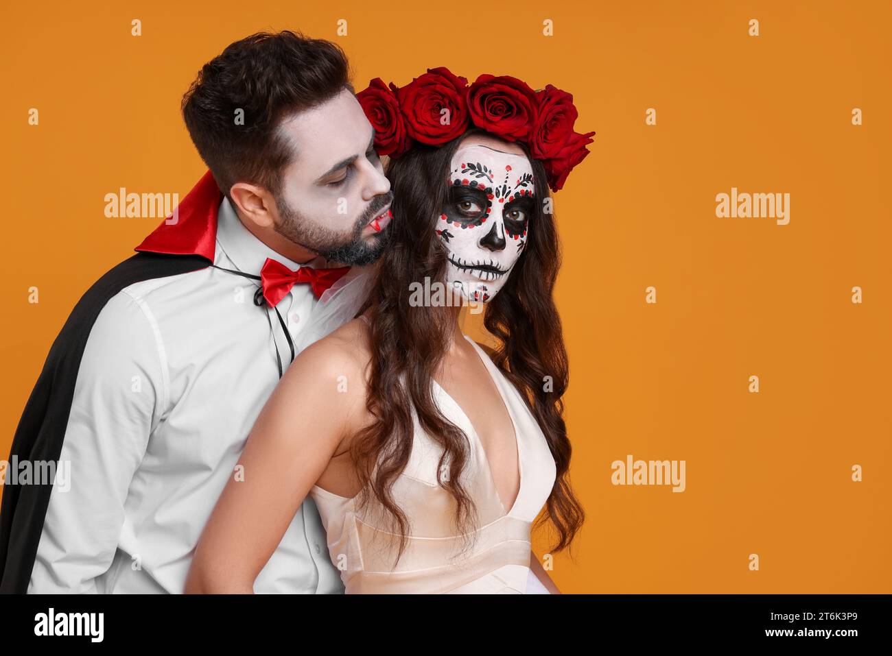 Couple in scary bride and vampire costumes on orange background, space for text. Halloween celebration Stock Photo