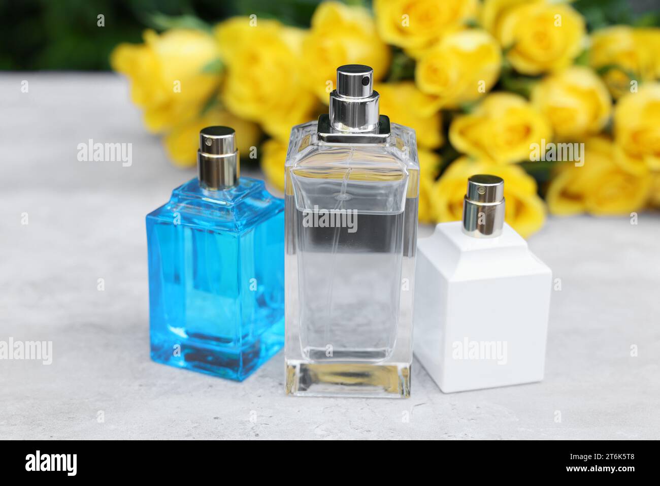 Perfumes and beautiful bouquet of yellow roses on light table, selective focus Stock Photo