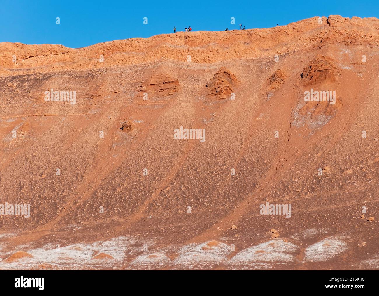 Tall cliff face in the Valle de la Luna in the Atacama Desert, Chile. Tourists at the top for scale. Stock Photo