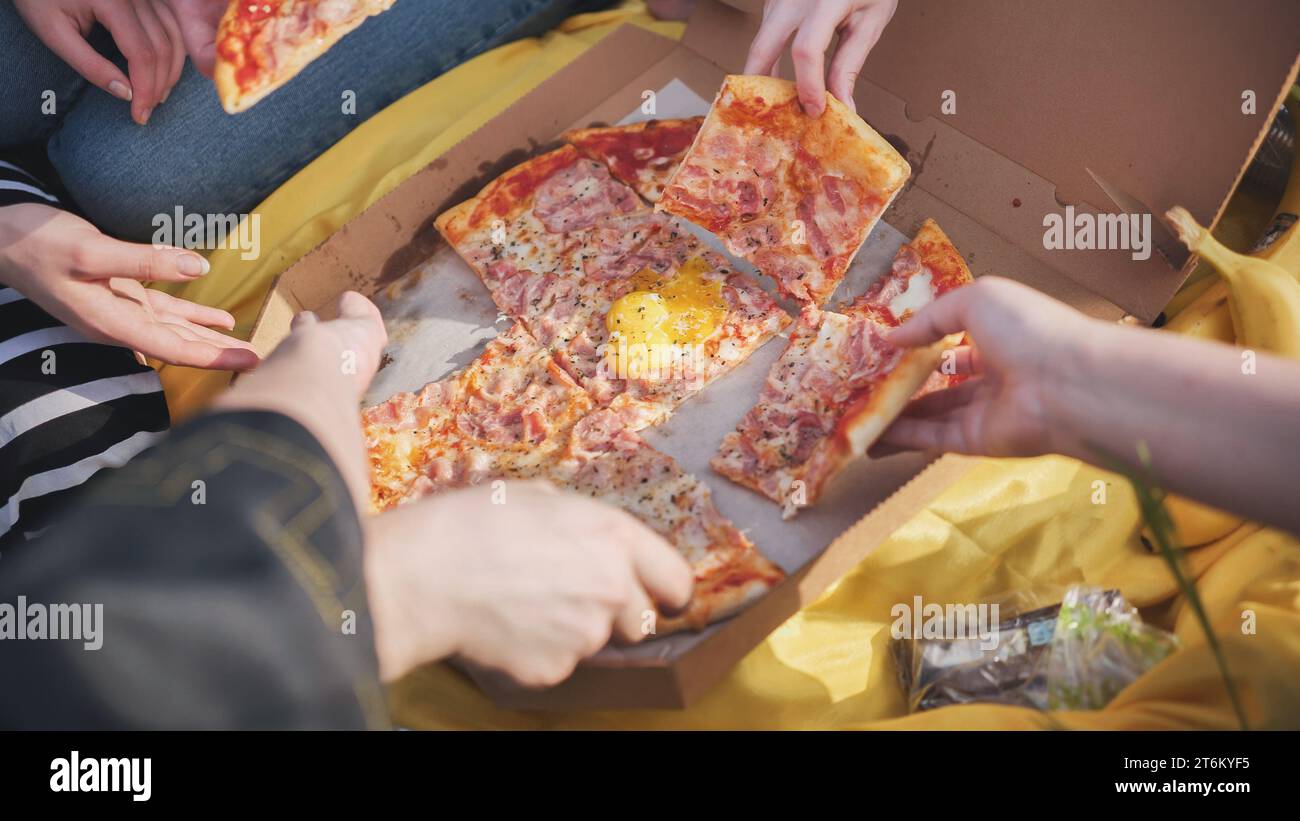 Young students' hands reach for the pizza. Stock Photo