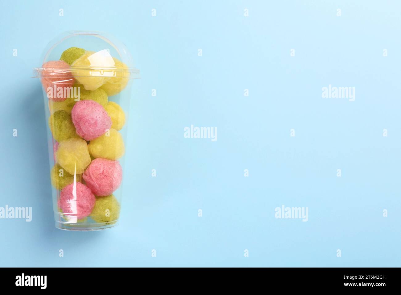 Plastic cup with color cotton balls on light blue background, top view and space for text. Sweet candy Stock Photo