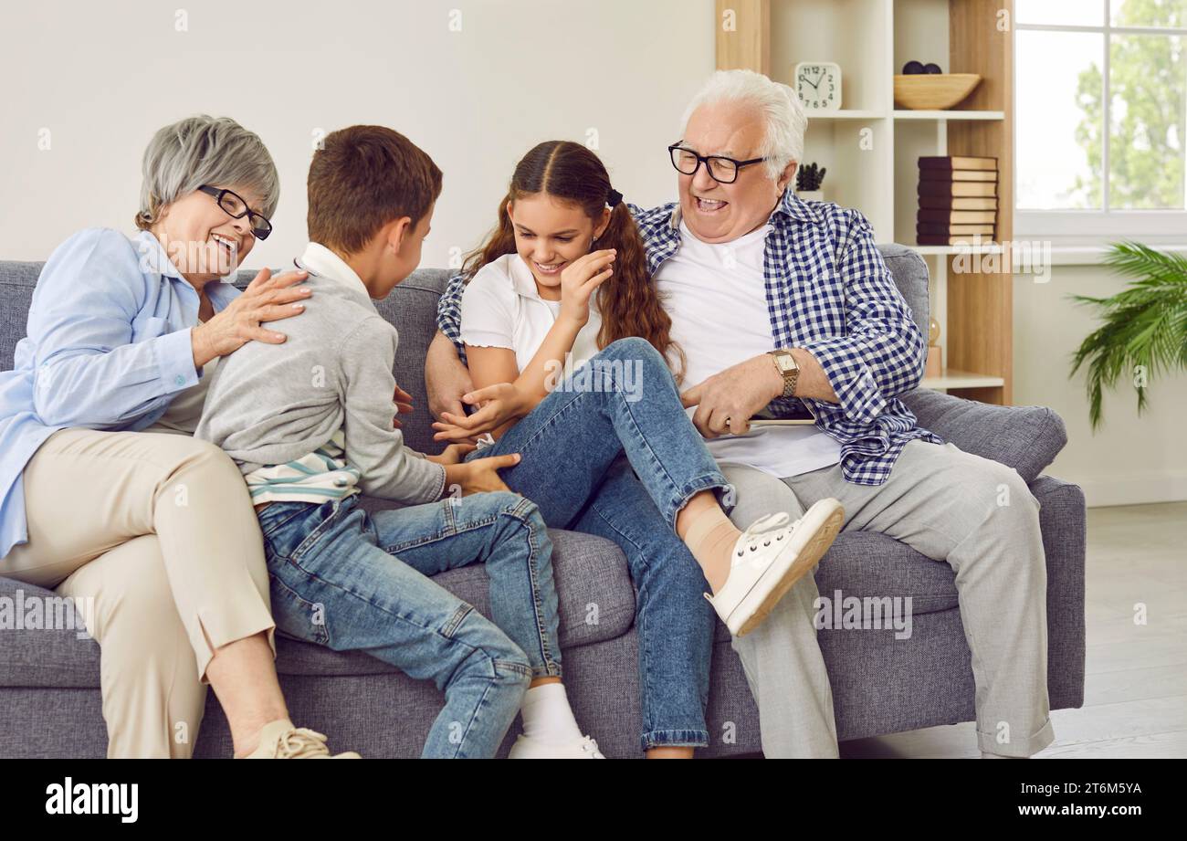 Happy grandparents tickling grandchildren while sitting on the sofa all together Stock Photo