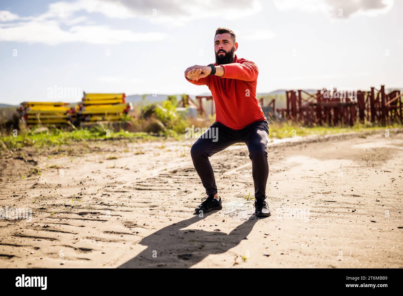 Young man is exercising outdoor. He is doing squats. Stock Photo