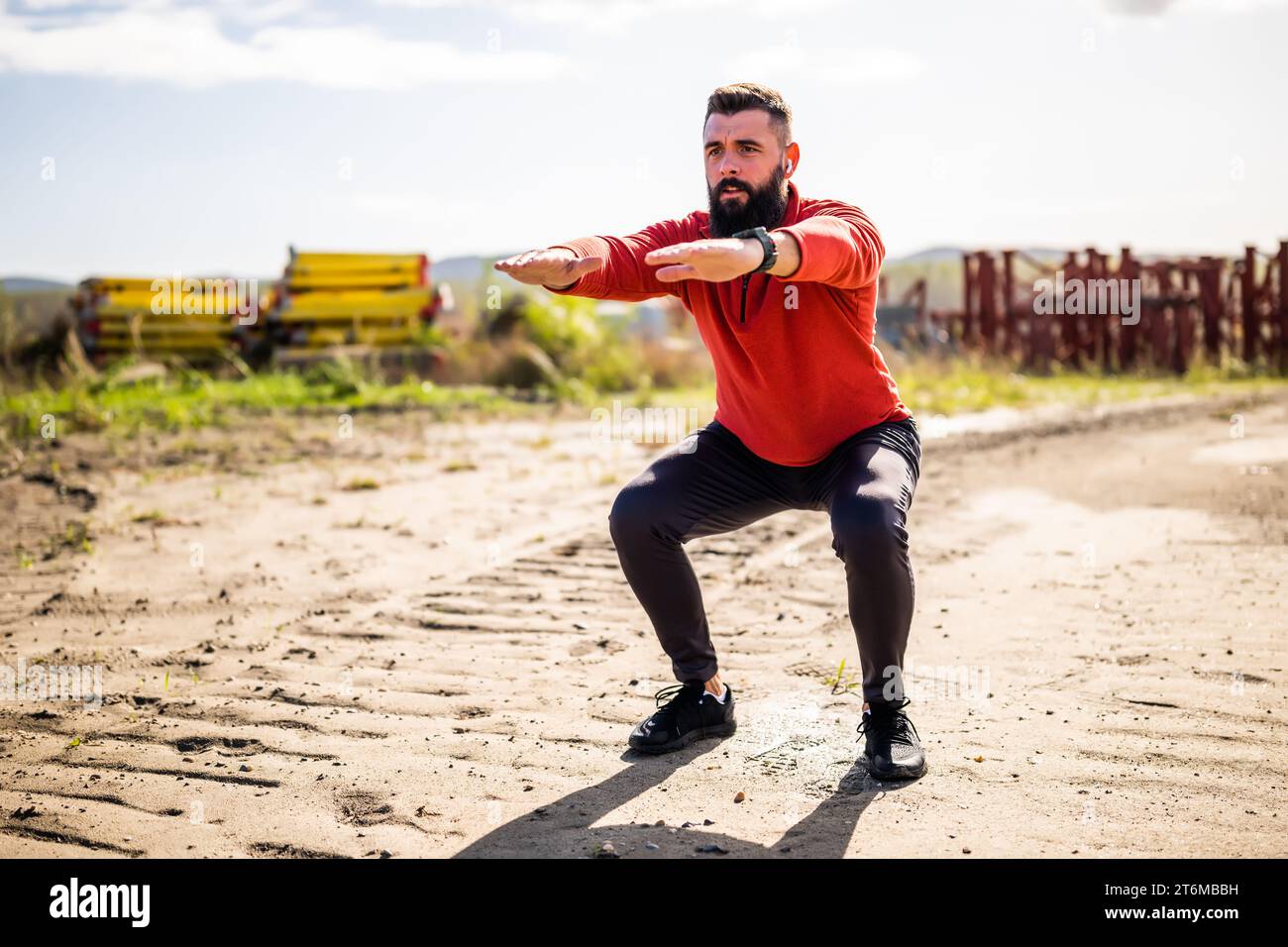 Young man is exercising outdoor. He is doing squats. Stock Photo