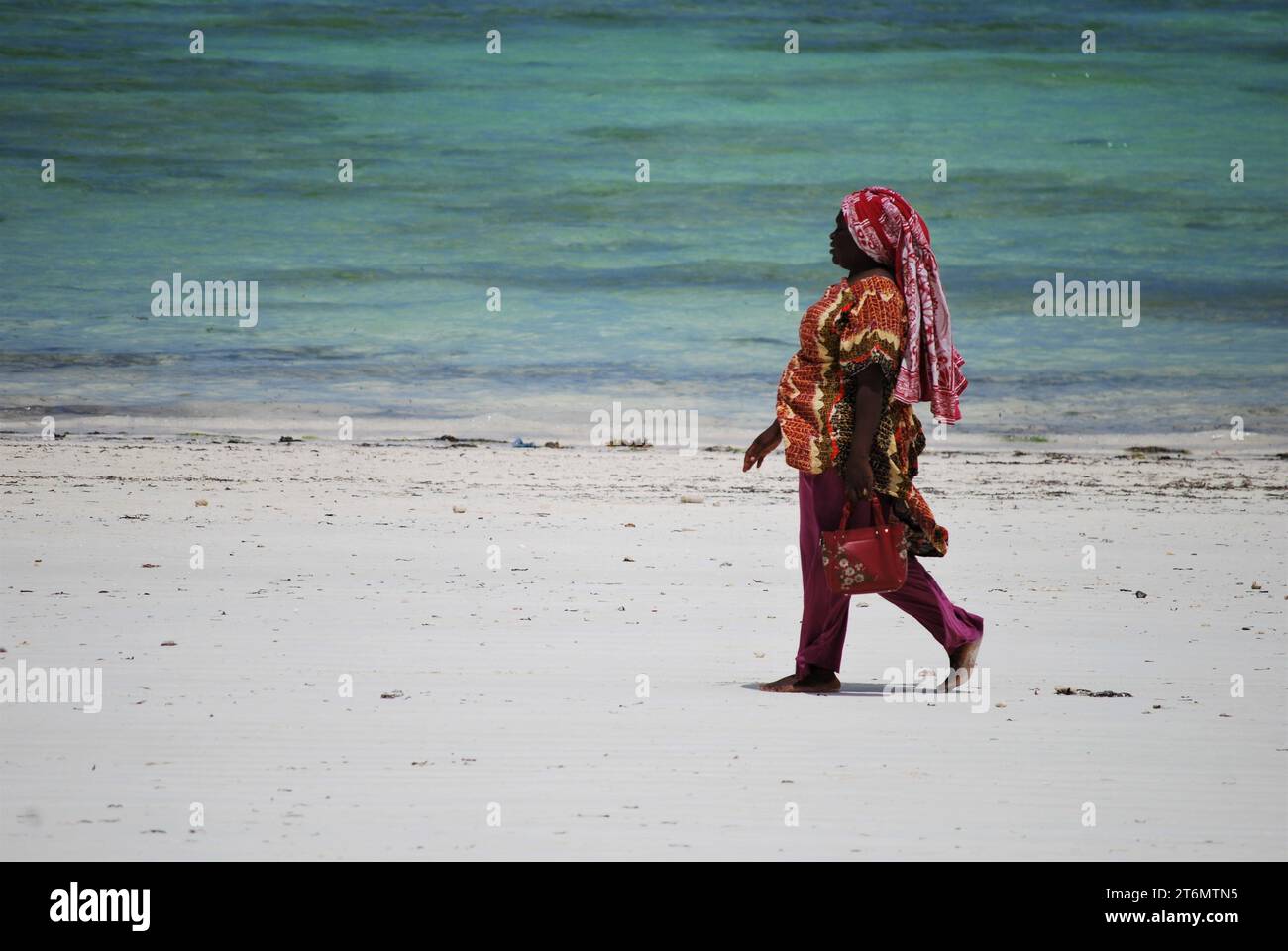 Local woman walking on the beach, in traditional dress, Paje Beach, Zanzibar, Unguja, Tanzania Stock Photo