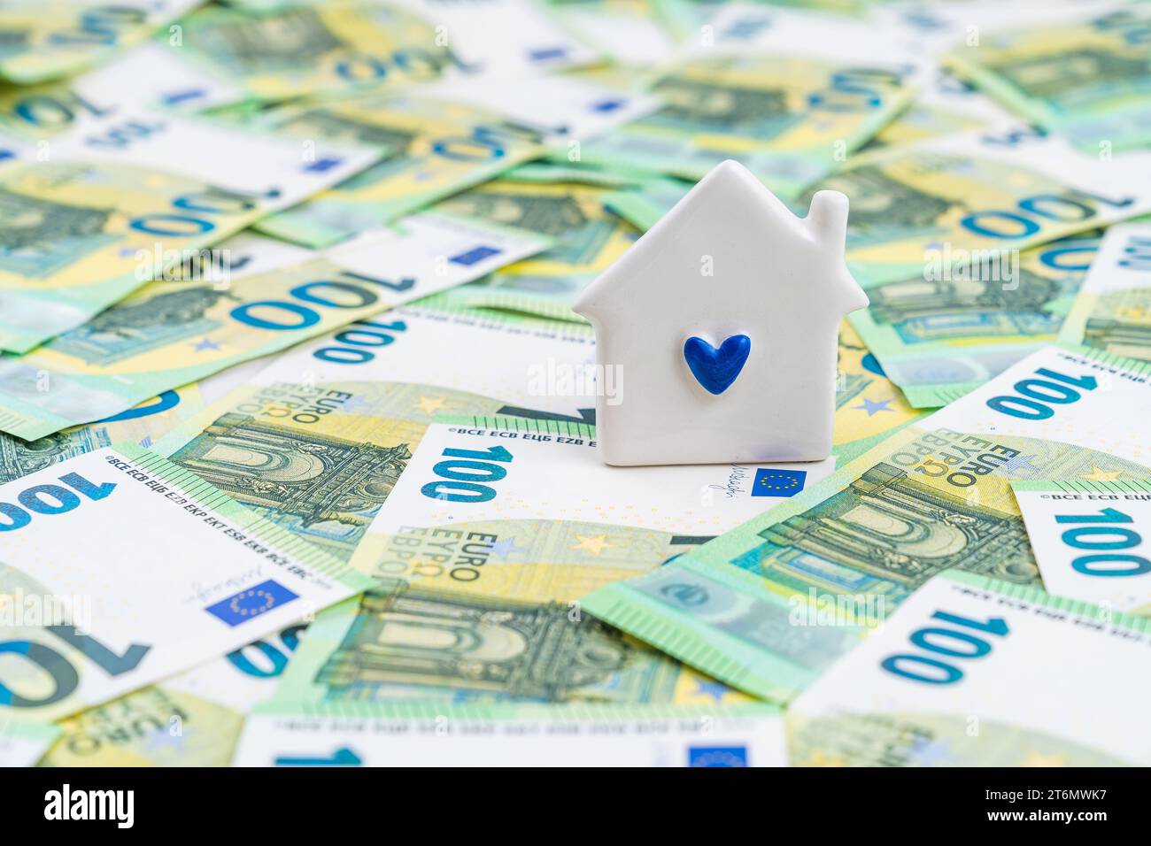 A little white house with a blue heart over many 100 euro banknotes, home investment concept. High quality photo Stock Photo