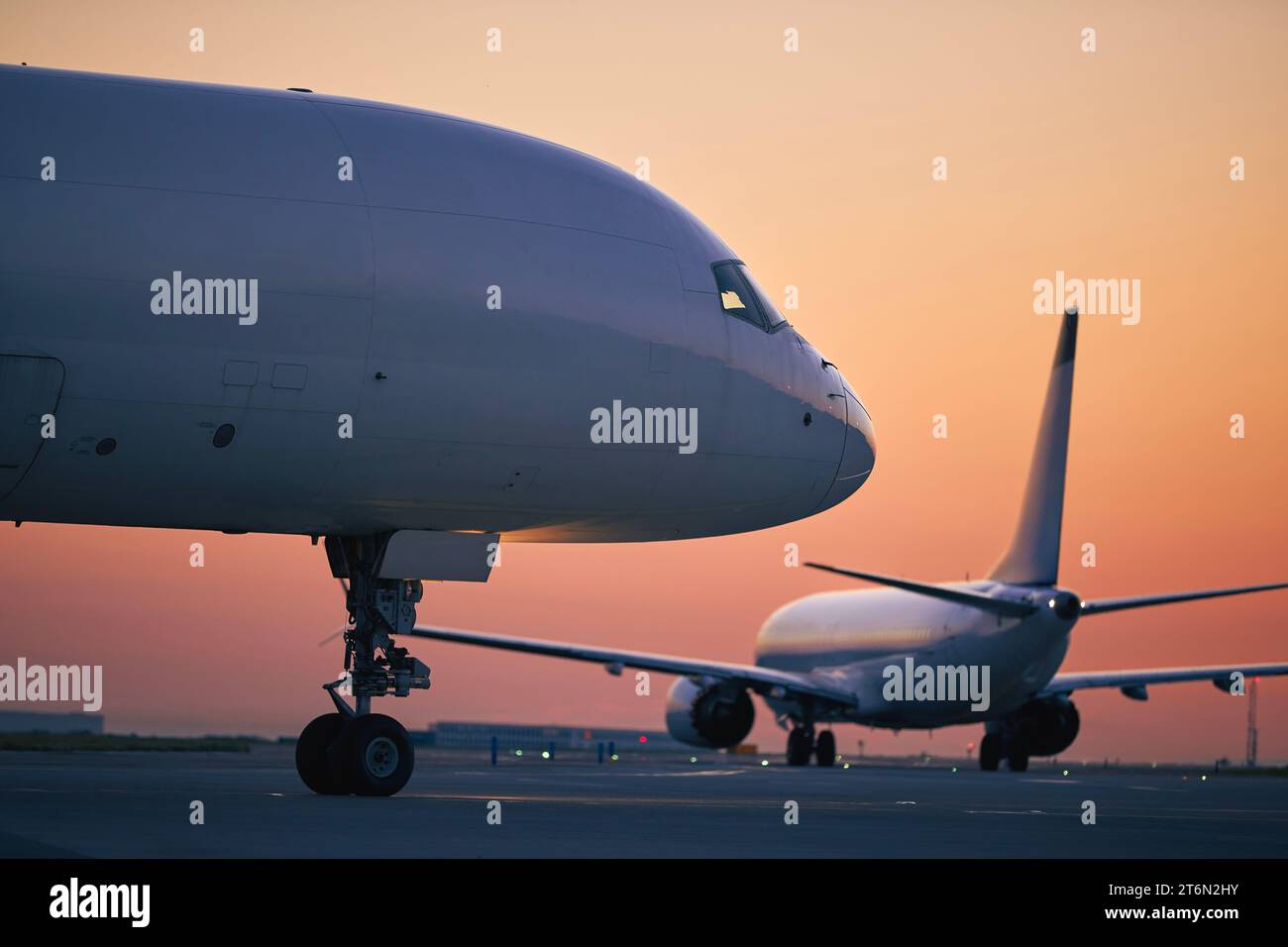Cargo airplane is taxiing behind passenger airplane during morning busy traffic to airport runway. Stock Photo