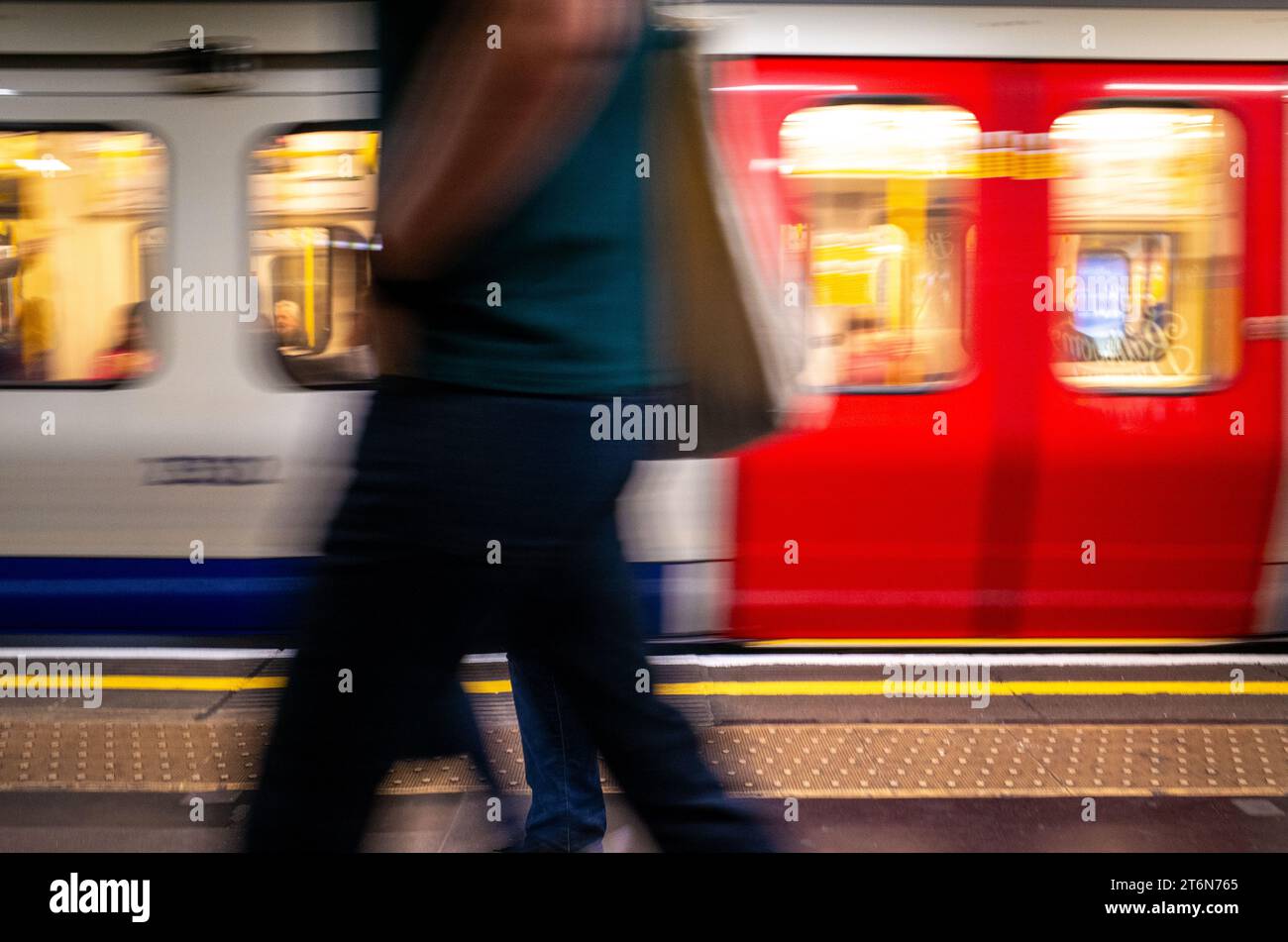 Motion blurred people pass in front of a moving London Underground tube train whilst walking on the station platform Stock Photo
