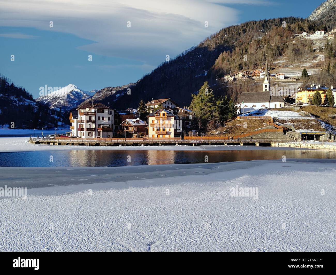 Alleghe church and houses in front of a partially frozen lake. Stock Photo