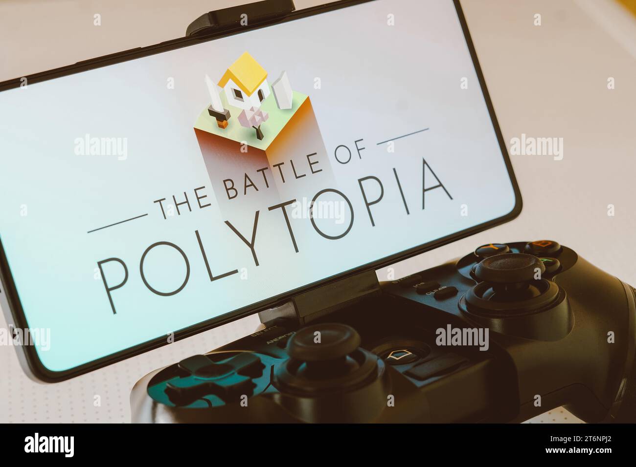 In this photo illustration, the Battle of Polytopia logo is displayed on a smartphone screen, next to a gamepad. Billionaire Elon Musk recently said that he calms his mind by playing this video game. Stock Photo