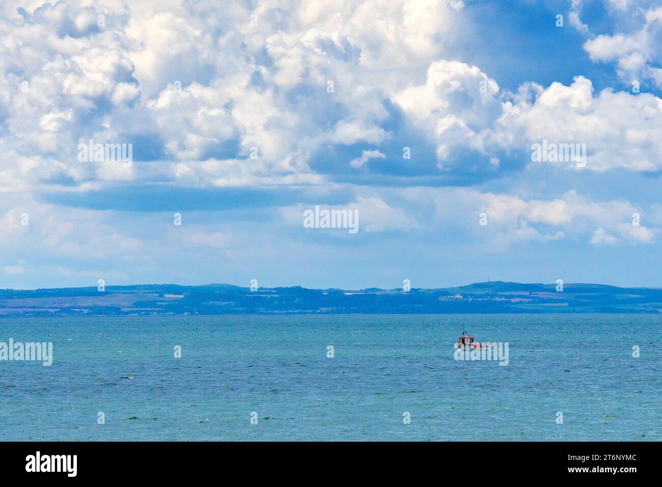 A small inshore fishing boat tending to its crab pots or creels off the east coast of Scotland, dwarfed by large summer cumulo-nimbus clouds. Stock Photo