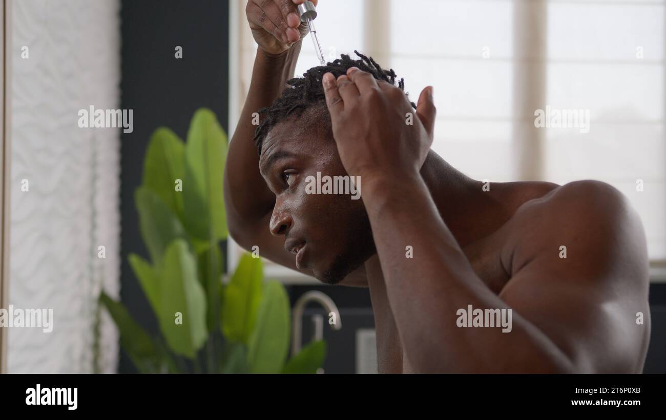 African American man applying argan oil serum on hair roots dreadlocks healthy massage morning bathroom routine male guy drip keratin cosmetic liquid Stock Photo