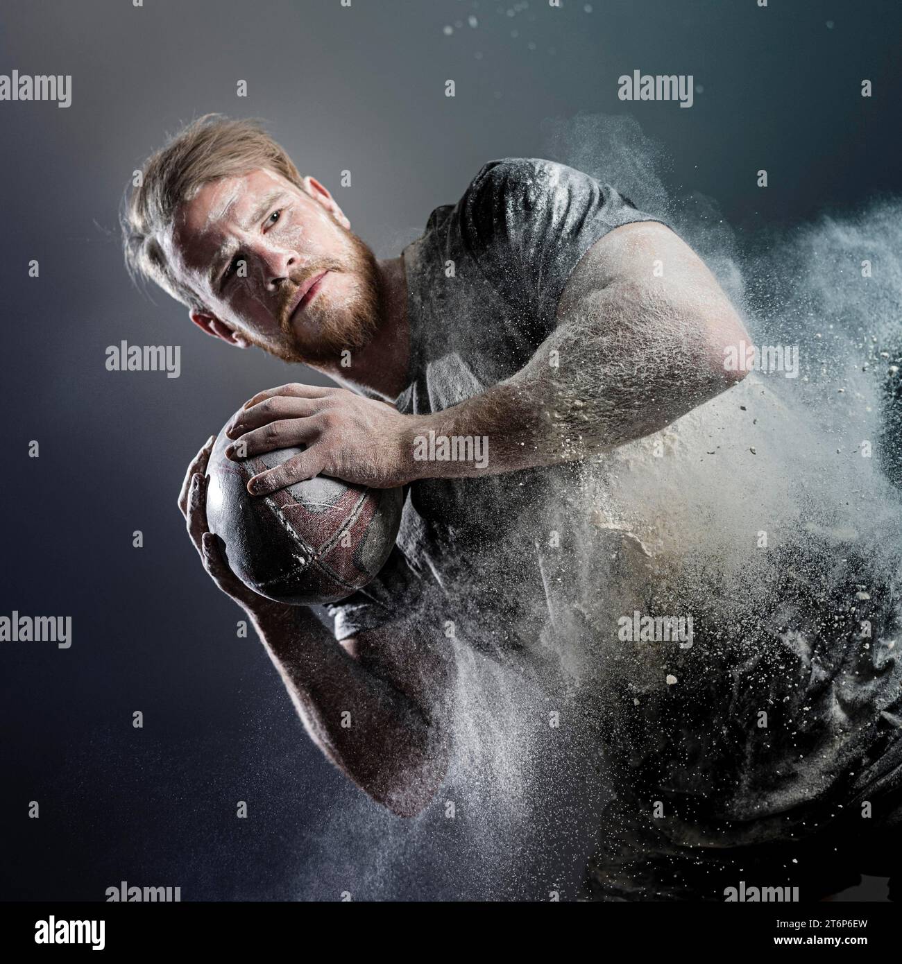Athletic male rugby player holding ball with dust Stock Photo