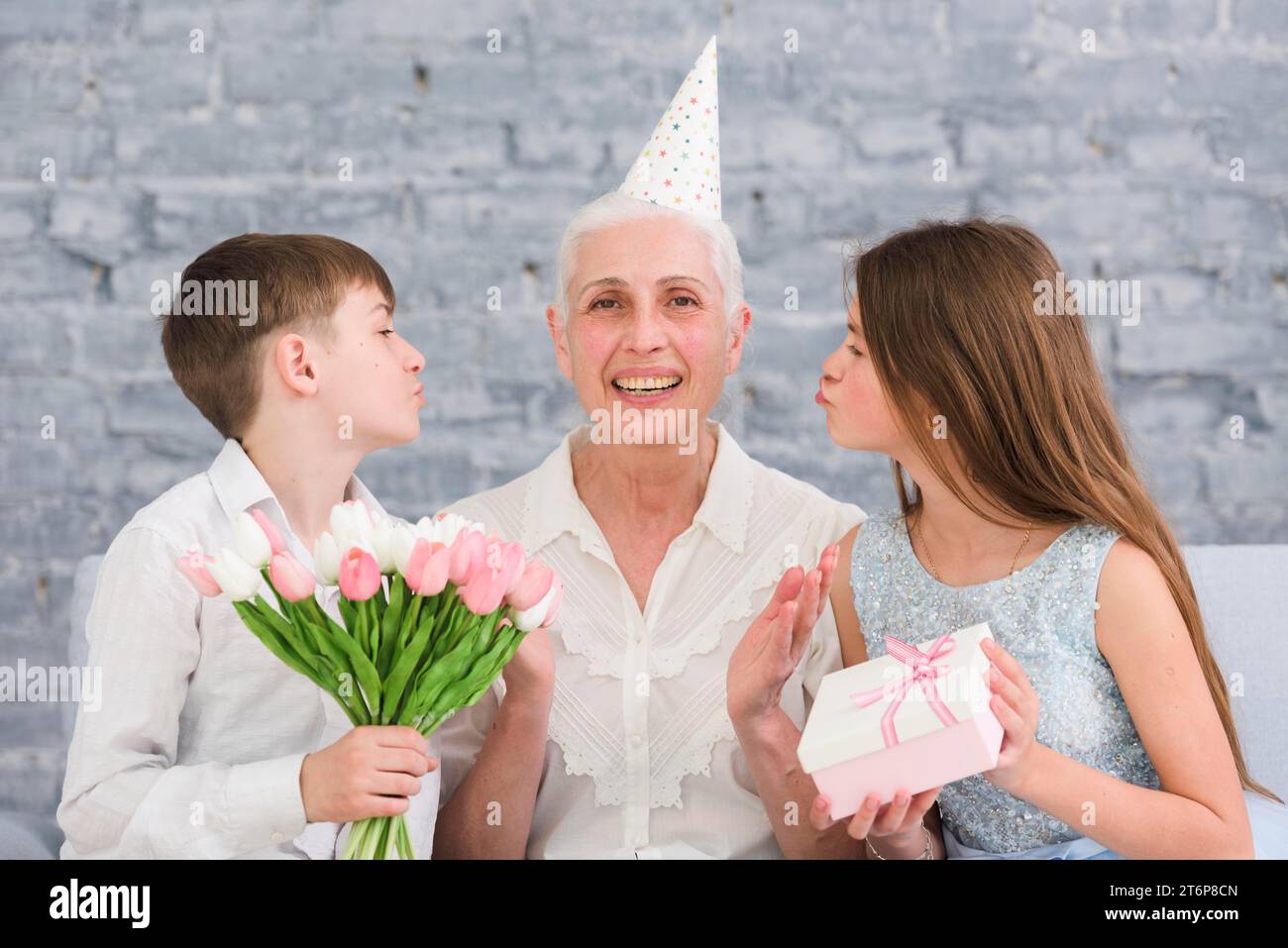 Joyful elder woman sitting her grandchildren with flowers bouquet gift box Stock Photo