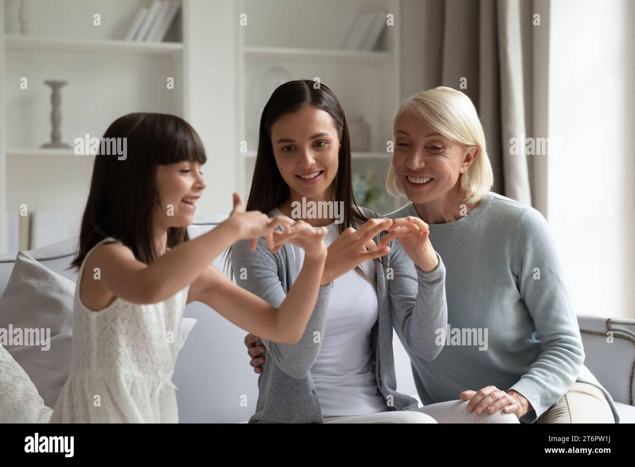 Smiling little girl with mother and grandmother practicing sign language Stock Photo